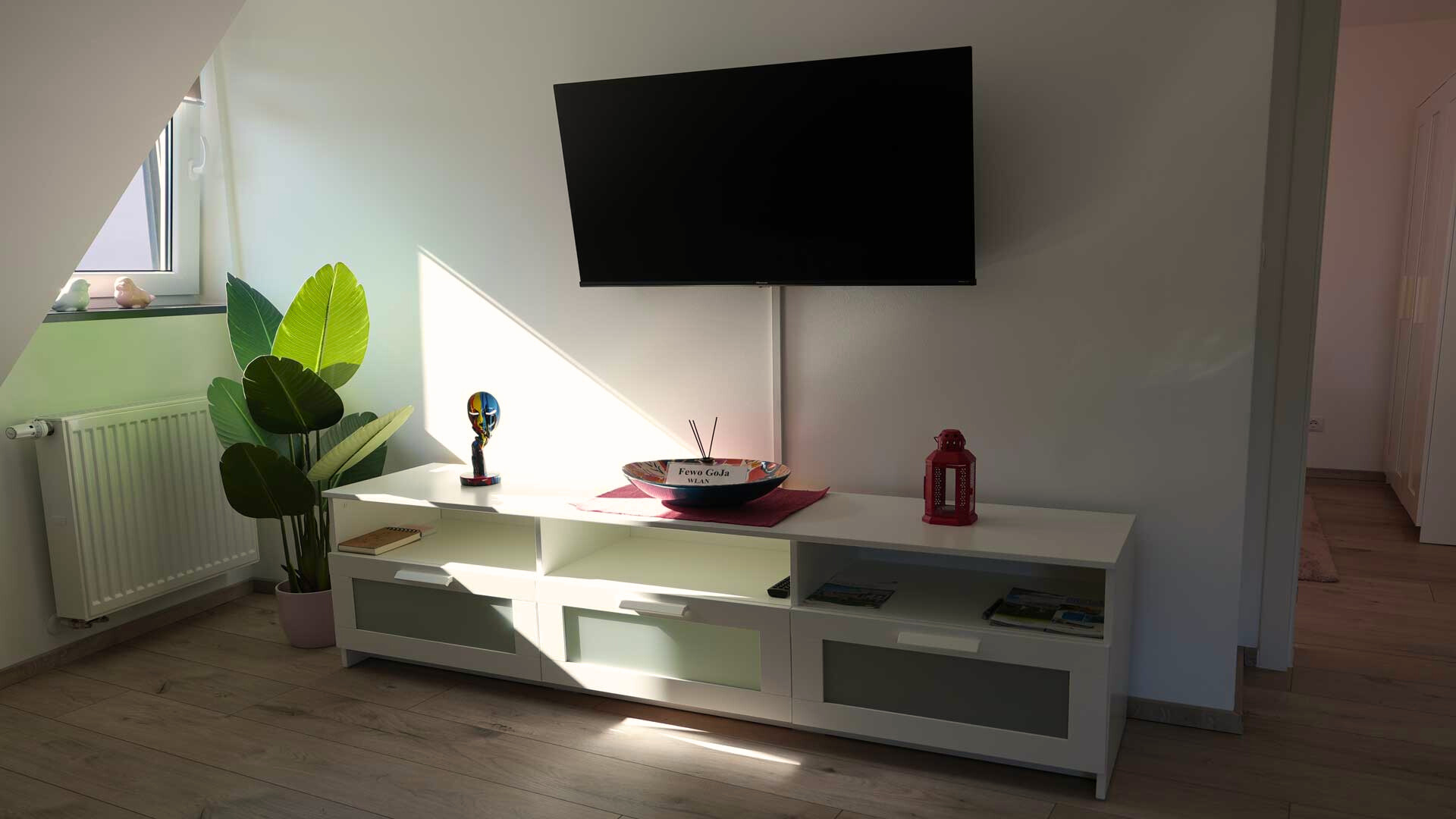 ferienwohnung-bad-koenigshofen-wohnzimmer-tv-bereich Wohnbereich einer Ferienwohnung in Bad Königshofen mit dekorativem TV-Board, Flachbildfernseher, Zimmerpflanze und stilvollen Accessoires.