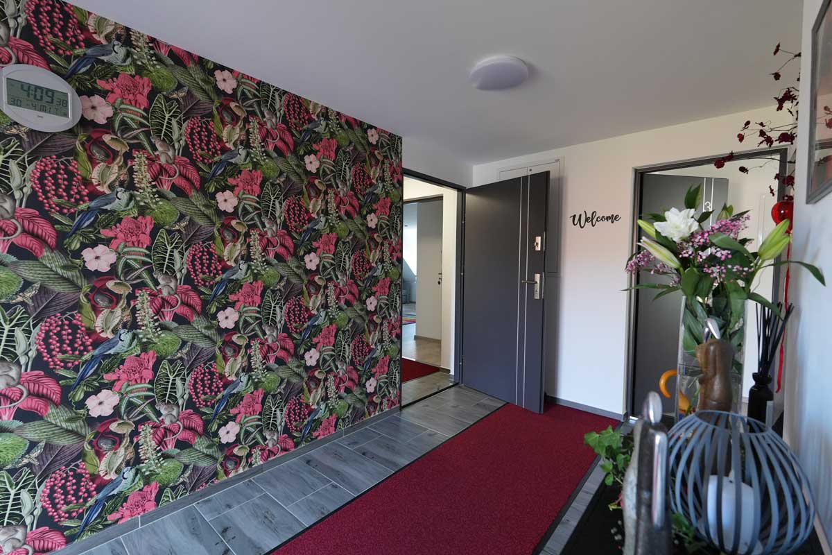 Moderner Flur einer Ferienwohnung mit floraler Akzentwand, rotem Teppichläufer und stilvoller Dekoration.