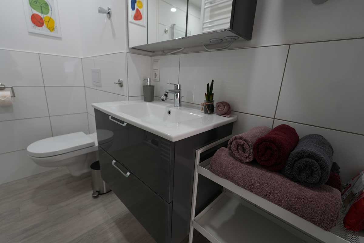 Modernes Badezimmer mit Waschbecken, Spiegel und Handtüchern in der Ferienwohnung GoJa