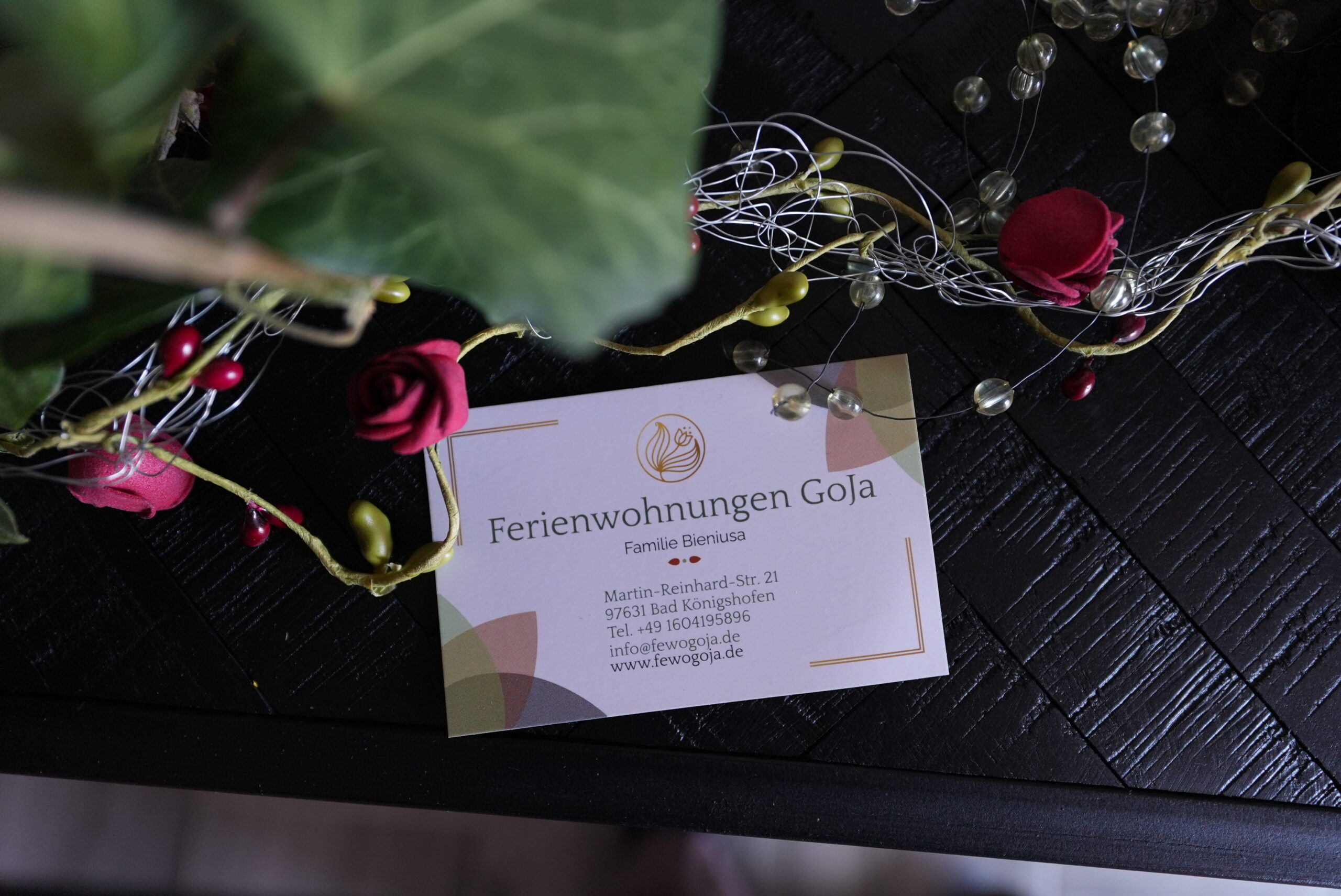 Visitenkarte von Ferienwohnungen GoJa auf dunklem Holztisch mit dekorativer Blumenumrahmung