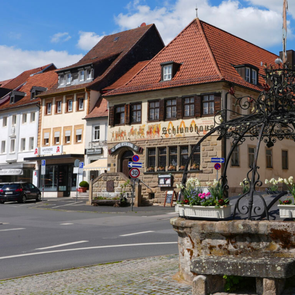 Historisches Schlundhaus am Marktplatz von Bad Königshofen mit Brunnen im Vordergrund bei blauem Himmel