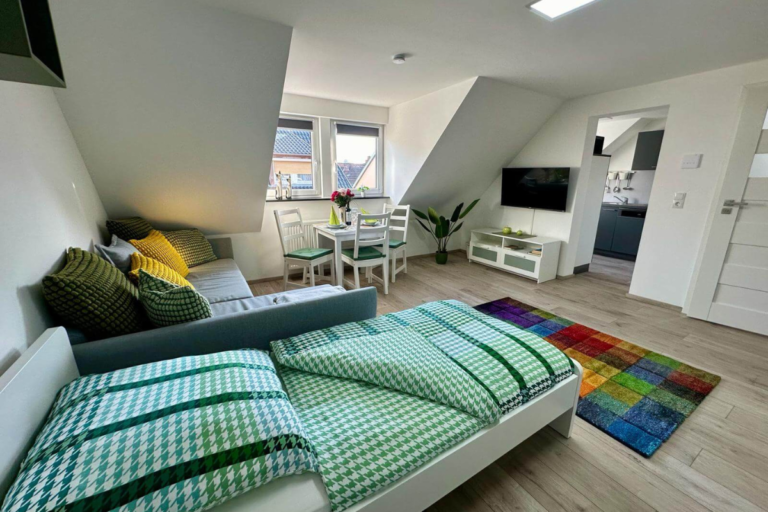 Wohn- und Schlafbereich mit Einzelbett und grauer Couch unter der Dachschräge