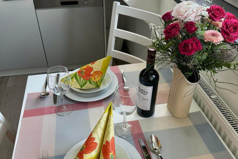 Liebevoll gedeckter Esstisch mit bunten Servietten, Rotwein, Gläsern und einem frischen Blumenstrauß – einladend für ein gemütliches Essen zu zweit.