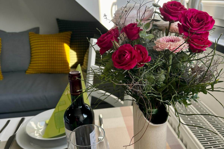 Tischdeko mit frischen Rosen, einer Flasche Rotwein und liebevoll gefalteter Serviette – ein herzliches Willkommen für die Gäste der Ferienwohnung