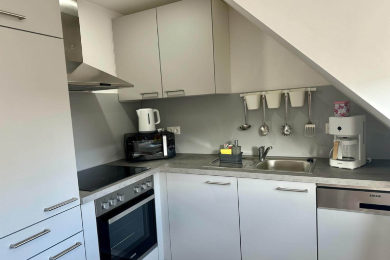 Voll ausgestattete Küchenzeile mit Herd, Spüle und Elektrogeräten unter der Dachschräge