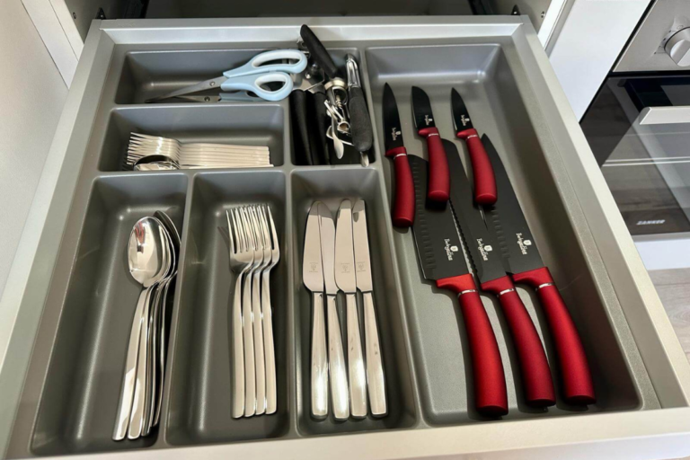 Ordentlich sortierte Besteckschublade mit vollständigem Set aus Löffeln, Gabeln, Messern sowie hochwertigen Küchenmessern, Schere und Korkenzieher – alles für die Selbstversorgung griffbereit.