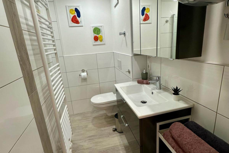 Modernes Badezimmer mit Waschbecken, Spiegel und Handtüchern in der Ferienwohnung GoJa