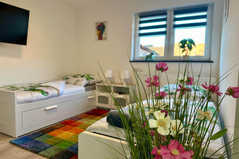 Geräumige, barrierearme Dusche mit Glastür und eleganten Fliesen – durch die offene Tür erkennbar der angrenzende Wohnbereich mit Esstisch und Stühlen.