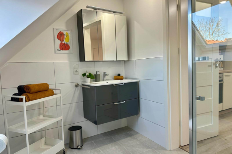 Stilvoll eingerichtetes Badezimmer mit Waschbecken, großem Spiegel, Handtuchregal und natürlichem Lichteinfall – hell, sauber und funktional gestaltet.